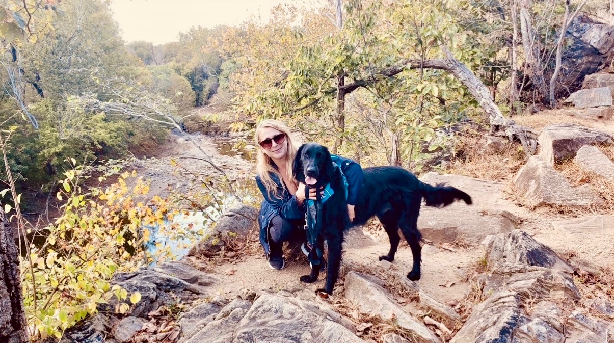 Ashley outdoors with a happy black dog on a rocky creek overlook
